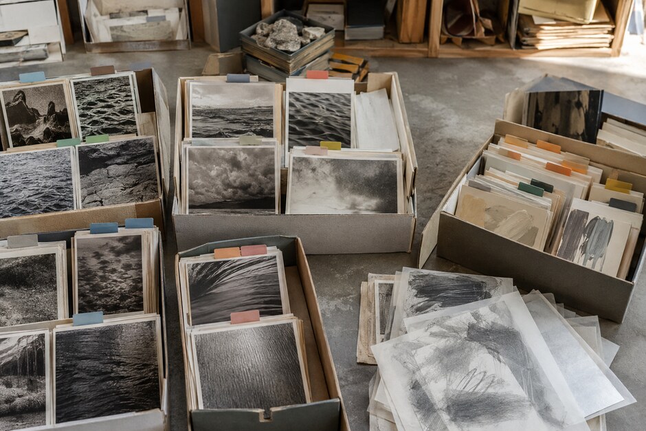 Open archive boxes containing original photographs, painted samples, sketches, and coloured index tabs.